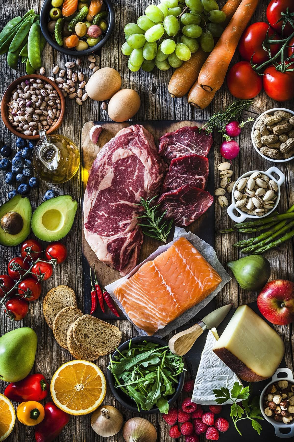 Overhead flat lay of salmon, steak, and fresh vegetables including asparagus, tomatoes, and carrots