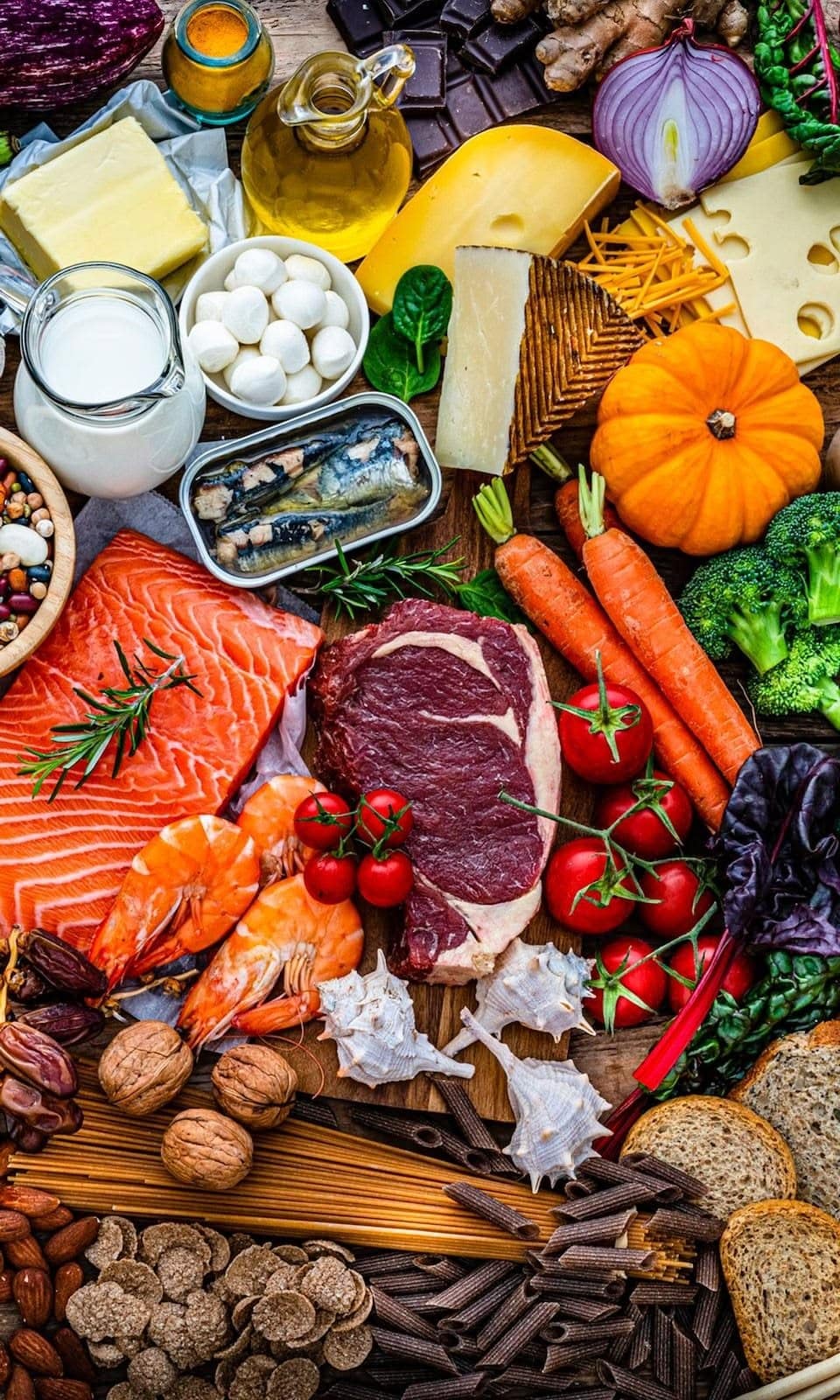 Overhead flat lay of steak, salmon, eggs, beans, and fresh vegetables, common high-protein whole foods